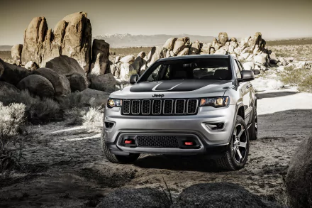 Silver Jeep Grand Cherokee SUV parked on a rugged off-road trail surrounded by large rocks, featured as an HD PC desktop wallpaper and background.