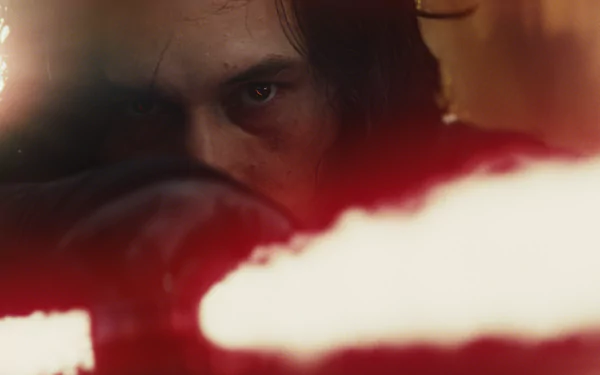 Close-up of a hooded, brooding figure igniting a red crossguard lightsaber in a cinematic scene from Star Wars: The Last Jedi — HD desktop wallpaper.