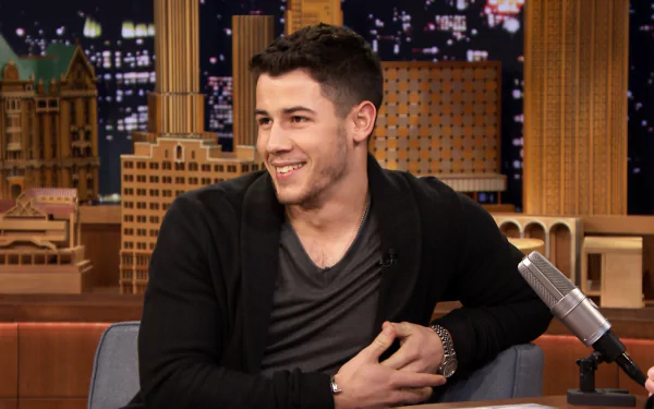 HD desktop wallpaper and background featuring a smiling man sitting in a talk show setting with city lights behind him.
