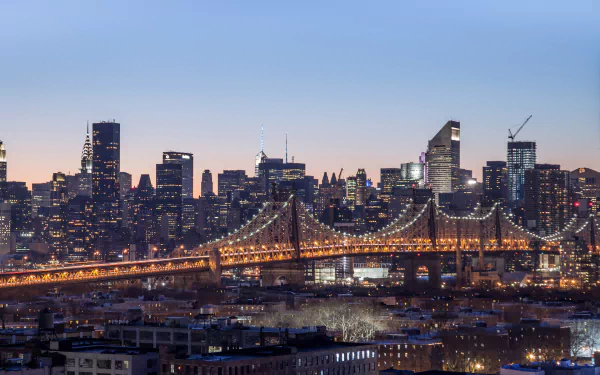 Queensboro Bridge lit at dusk with Manhattan skyscrapers rising behind, New York City skyline, man-made urban panorama, USA; 2K Quad HD PC desktop wallpaper and background.