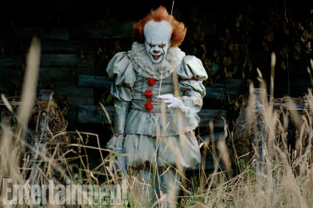 HD desktop wallpaper of Pennywise from the movie It (2017), showing the character in his iconic clown costume, standing amidst tall grass with a house in the background.
