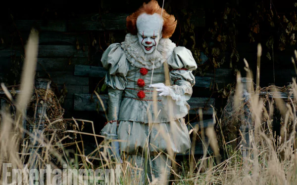 HD desktop wallpaper of Pennywise from the movie It (2017), showing the character in his iconic clown costume, standing amidst tall grass with a house in the background.