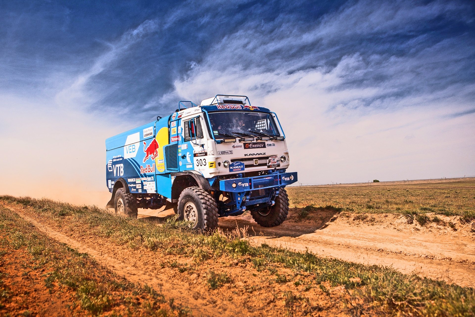 HD PC desktop wallpaper featuring a rallying sports vehicle racing on a dusty off-road track under a dynamic cloudy sky.