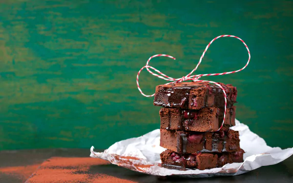 Stacked chocolate brownies tied with red and white string on crumpled parchment, set against a textured green background, captured in a 4K Ultra HD still life image.