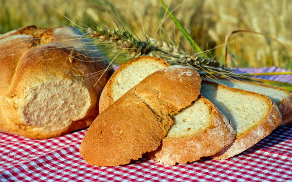 Rustic sliced loaf and whole bread on a red gingham cloth with wheat stalks — baking and food scene, high-resolution 4K Ultra HD PC desktop wallpaper background.