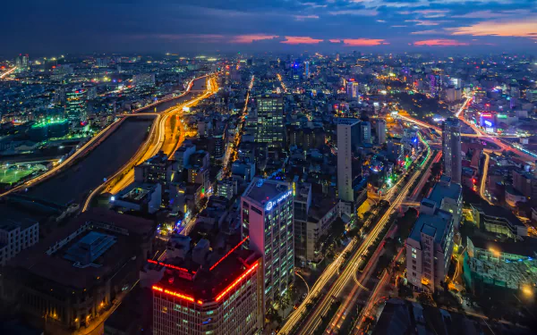 A vibrant night time lapse of Ho Chi Minh City with illuminated buildings and streets along the Saigon River in Vietnam, captured in HD for a desktop background.