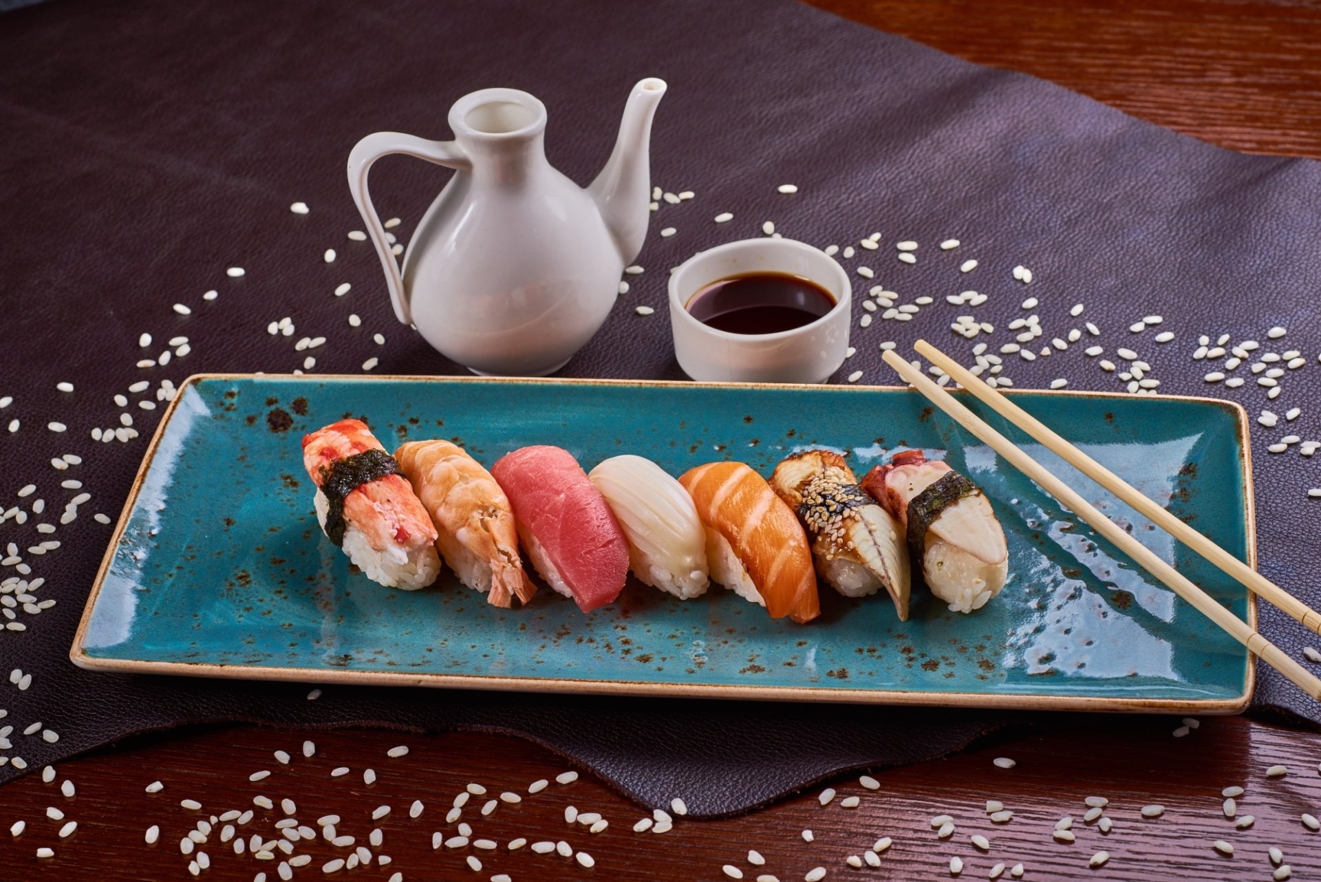 HD PC desktop wallpaper: still-life sushi platter of assorted fish nigiri on a turquoise plate with chopsticks, scattered rice, soy sauce cup and sake pitcher — seafood, food background.