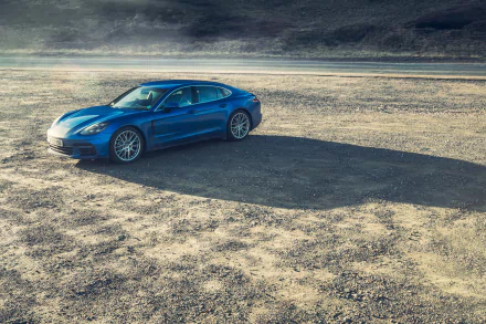 Blue Porsche Panamera Turbo on a sunlit desert road, casting a long shadow — 4K Ultra HD PC desktop wallpaper/background of the vehicle.
