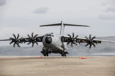 A high-definition wallpaper featuring the Airbus A400M military transport aircraft taking off from a runway, with mountains and a cloudy sky in the background.