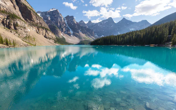 Crystal-clear waters of Moraine Lake in Canada reflect towering mountains and blue sky, showcasing stunning natural beauty in this 4K Ultra HD desktop wallpaper.