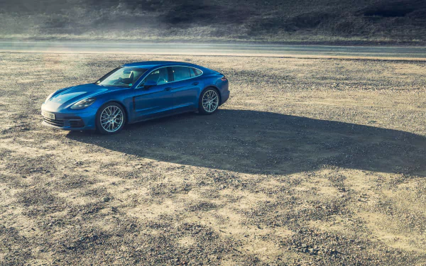 Blue Porsche Panamera Turbo on a sunlit desert road, casting a long shadow — 4K Ultra HD PC desktop wallpaper/background of the vehicle.