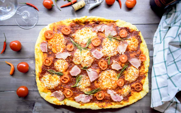 HD PC desktop wallpaper: food still life — overhead of a rustic tomato pizza topped with mozzarella, cherry tomatoes, ham and rosemary on a wooden table with scattered peppers.