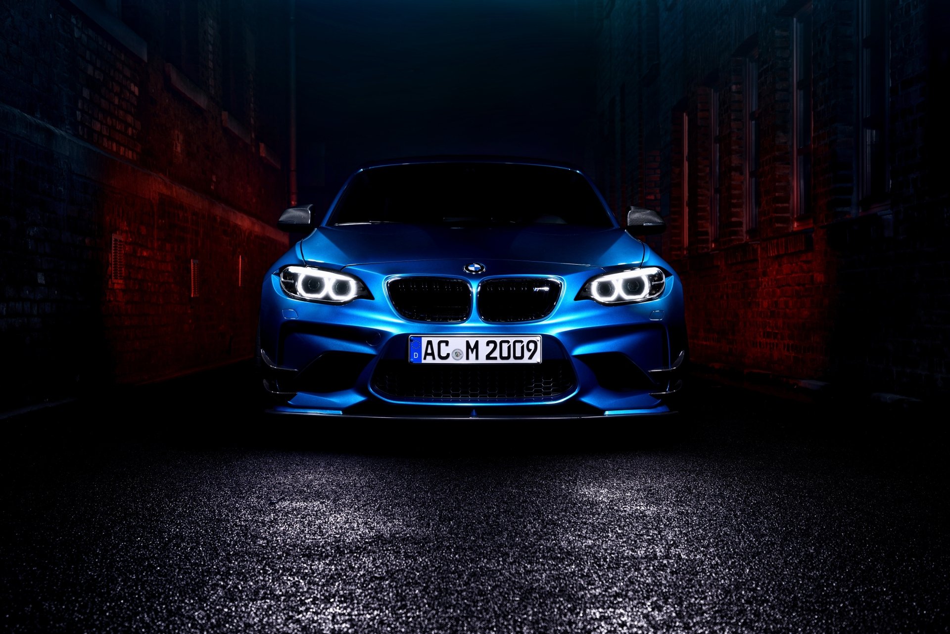 Front view of a blue BMW M2 with illuminated headlights, showcased as a 4K Ultra HD PC desktop wallpaper in a dark, urban setting.