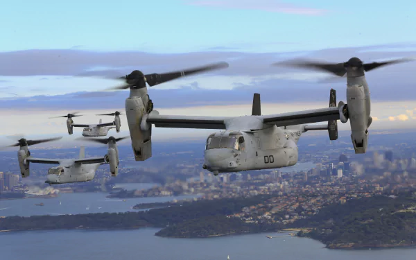 Two Bell Boeing V-22 Osprey military transport aircraft flying over a coastal cityscape under a cloudy sky, captured in 4K Ultra HD resolution.