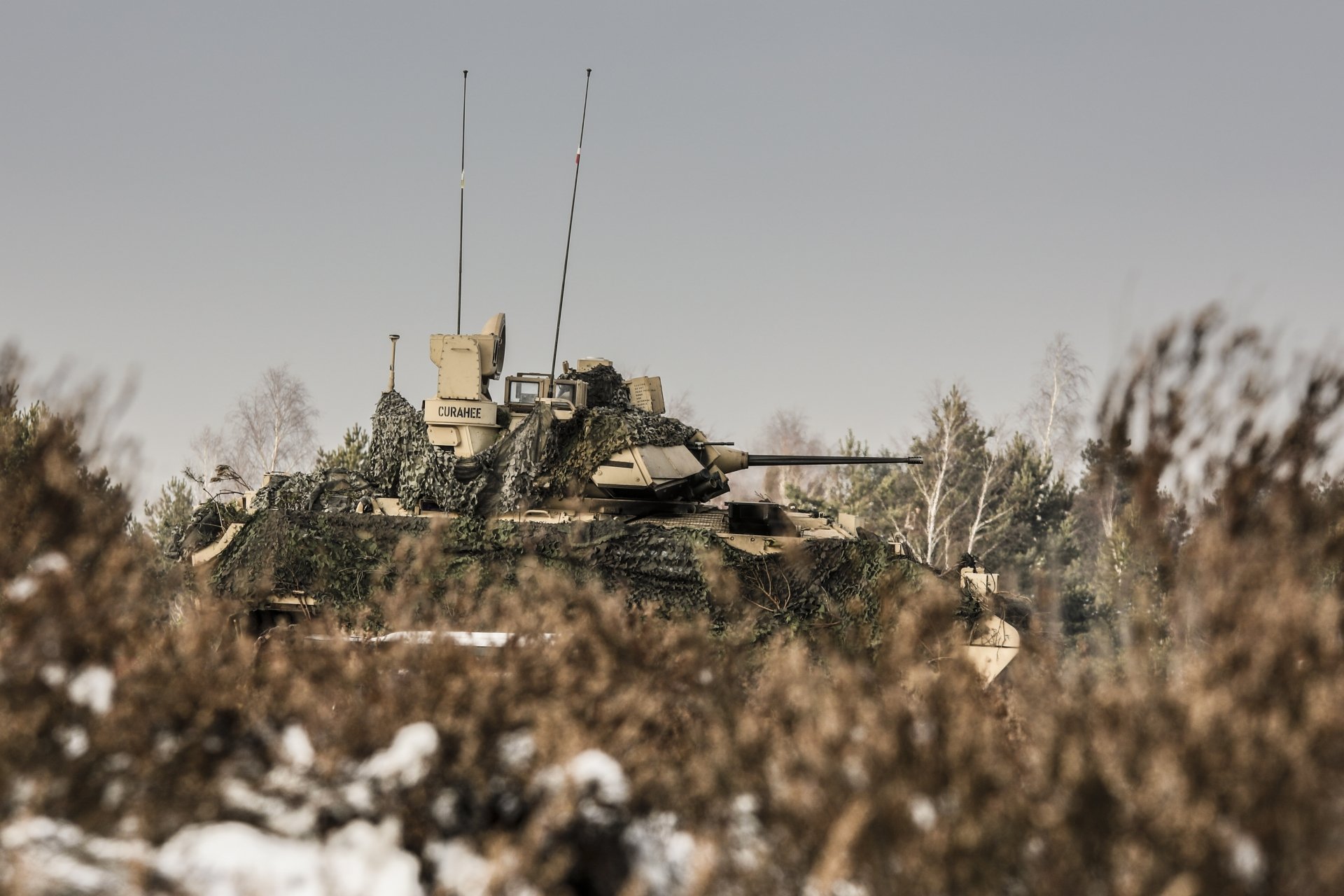 4K Ultra HD image of an M2 Bradley armored personnel carrier positioned in a snowy, wooded area, highlighting its military design and tactical features.