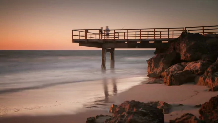 A fisherman stands on a man-made pier overlooking the calm sea at sunset, captured in this HD desktop wallpaper and background.