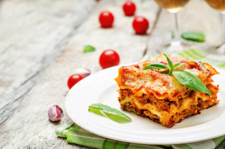 A close-up 4K Ultra HD still life of a slice of lasagna garnished with fresh basil, plated on white with cherry tomatoes scattered on a rustic wooden surface.
