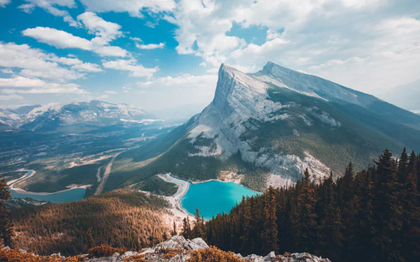 Panoramic view of a forested mountain landscape with a serene lake in the foreground. This HD desktop wallpaper and background captures the beauty of nature with its towering peaks and lush greenery.
