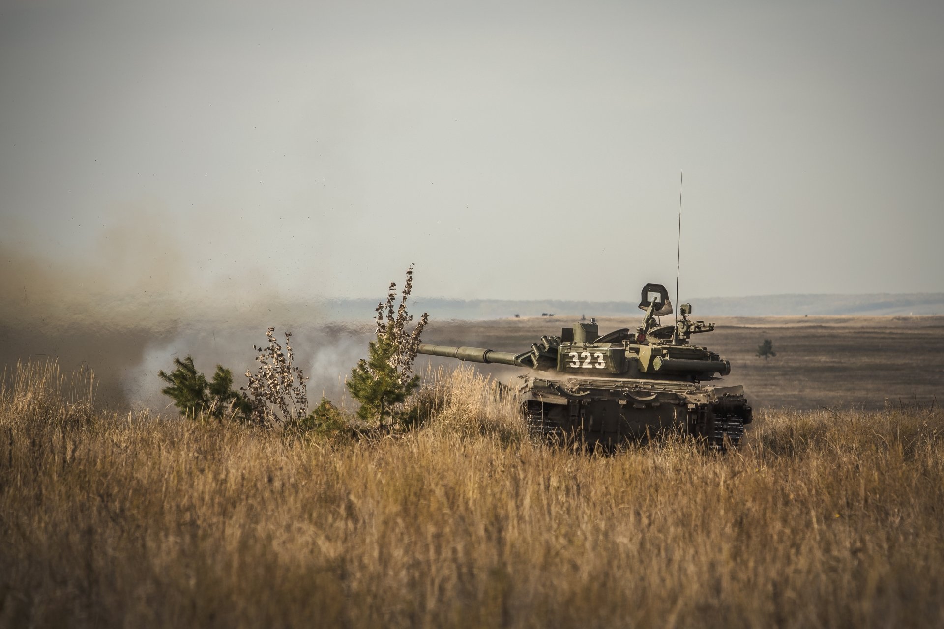 A T-90 military tank moves through a field, captured in 4K Ultra HD detail, set against a hazy, expansive landscape background.