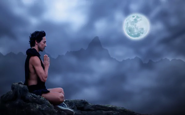 A person practices yoga meditation on a mountain at night under a glowing full moon, captured in stunning 4K Ultra HD photography.