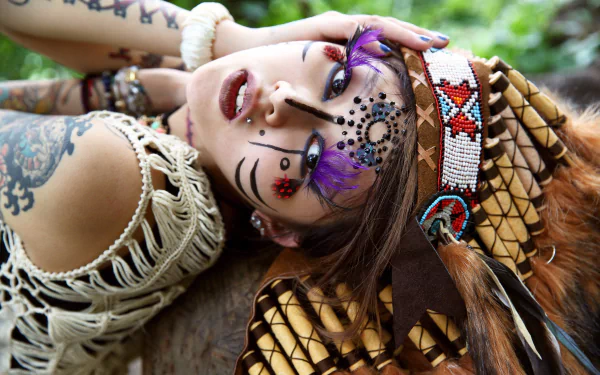 A Native American woman with brown eyes and face tattoos, wearing a traditional headdress and lipstick, captured in a detailed 4K Ultra HD desktop wallpaper.