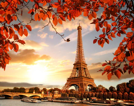 4K Ultra HD view of the Eiffel Tower in Paris framed by vibrant fall leaves under a dramatic sky, showcasing the iconic man-made monument in autumn.