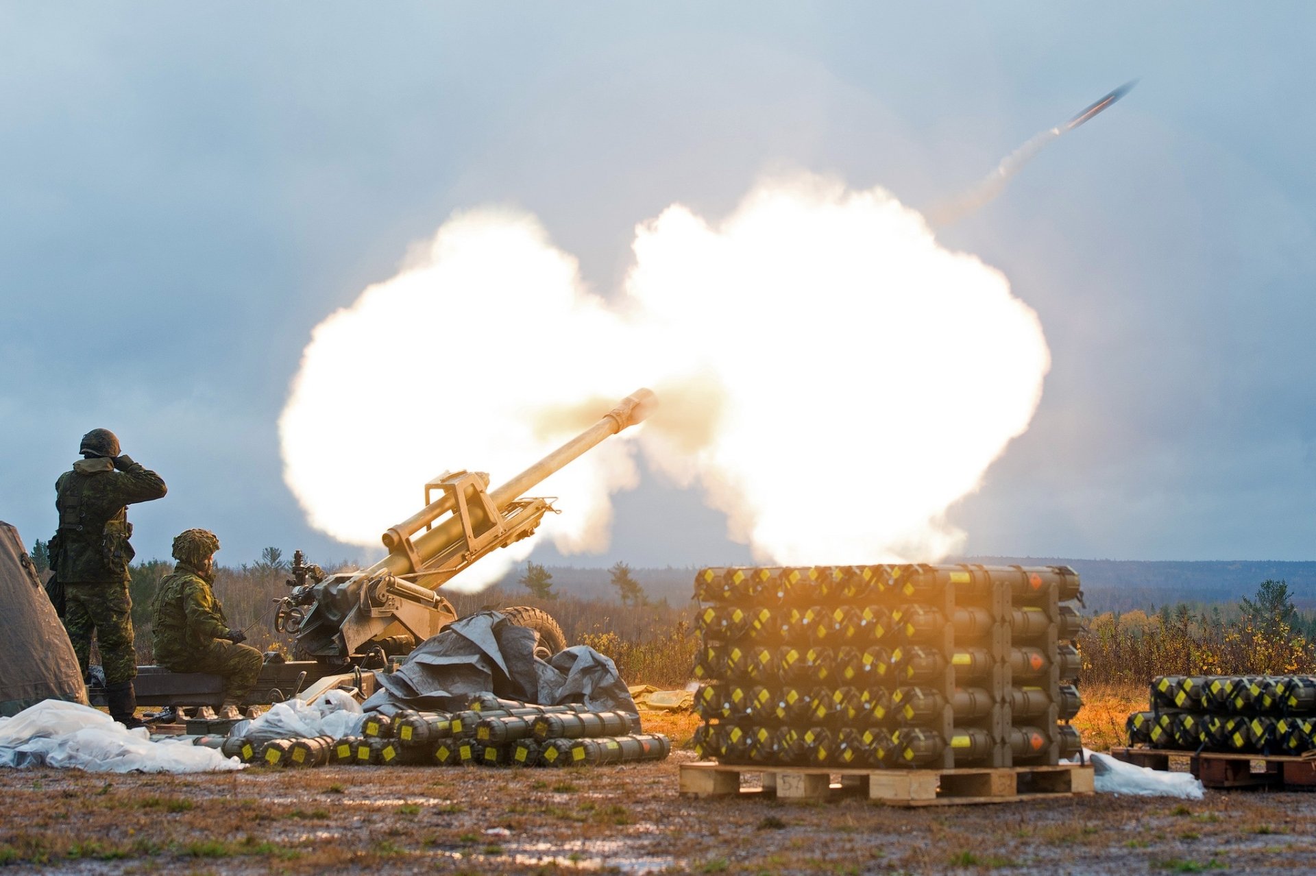 HD PC desktop wallpaper showing a soldier operating military artillery during a live firing exercise in an open field.