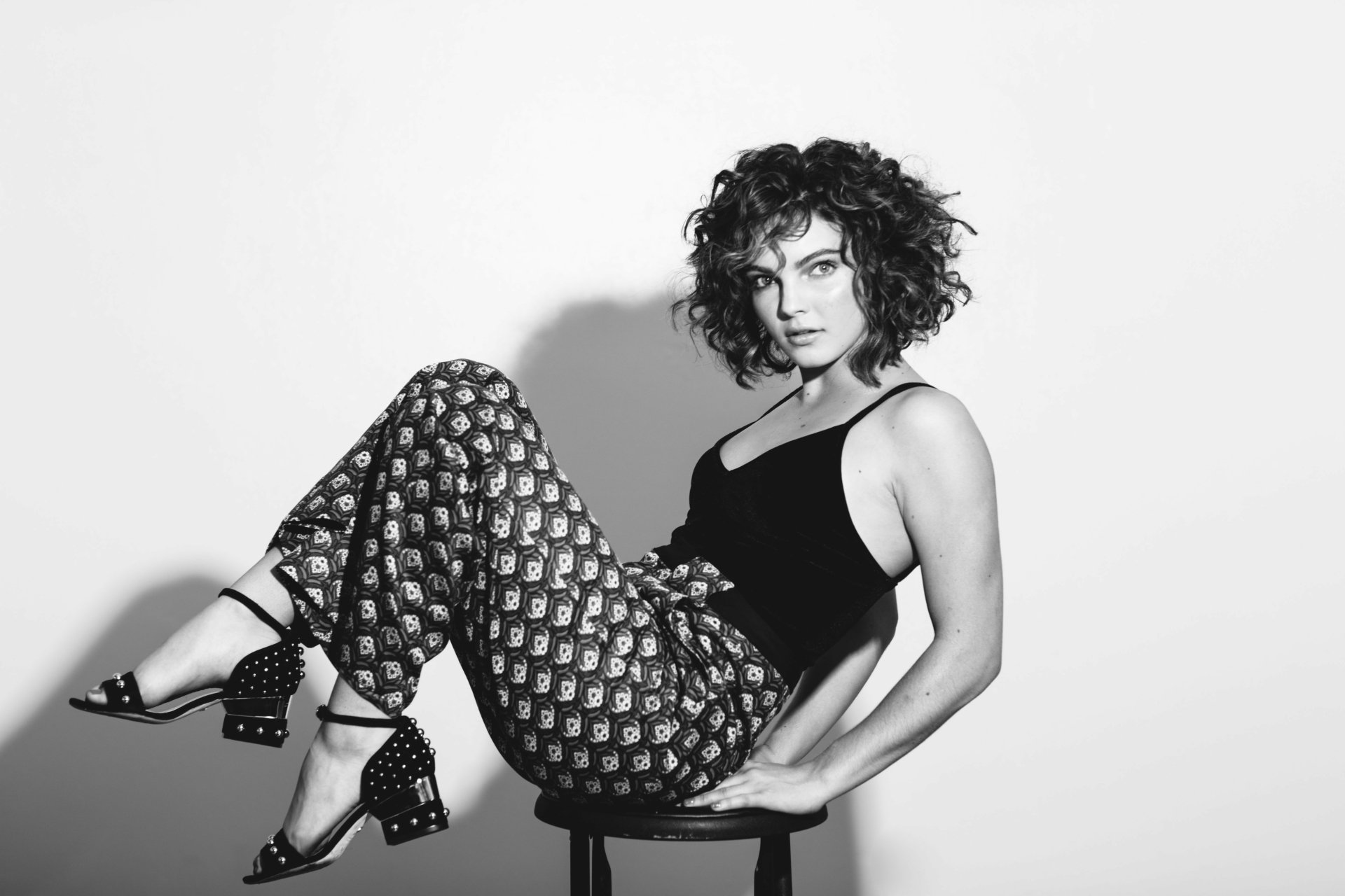 Black-and-white monochrome portrait of an actress (identity not disclosed), woman reclining on a stool in patterned pants — 4K Ultra HD PC desktop wallpaper.