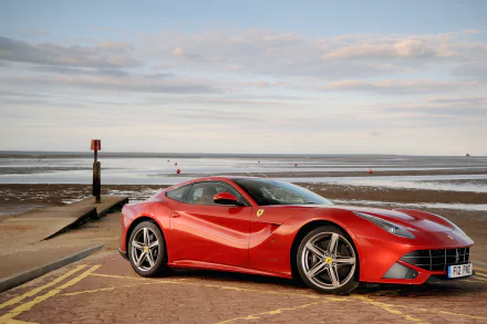 Red Ferrari F12berlinetta supercar parked on a seaside road at low tide, sleek sports car vehicle under a cloudy sky — 4K Ultra HD PC desktop wallpaper background.