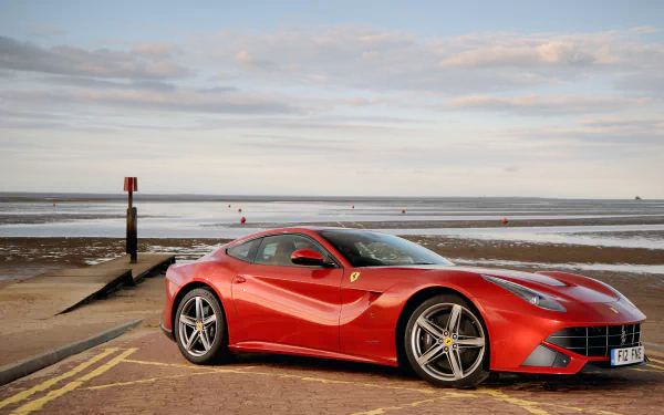 Red Ferrari F12berlinetta supercar parked on a seaside road at low tide, sleek sports car vehicle under a cloudy sky — 4K Ultra HD PC desktop wallpaper background.