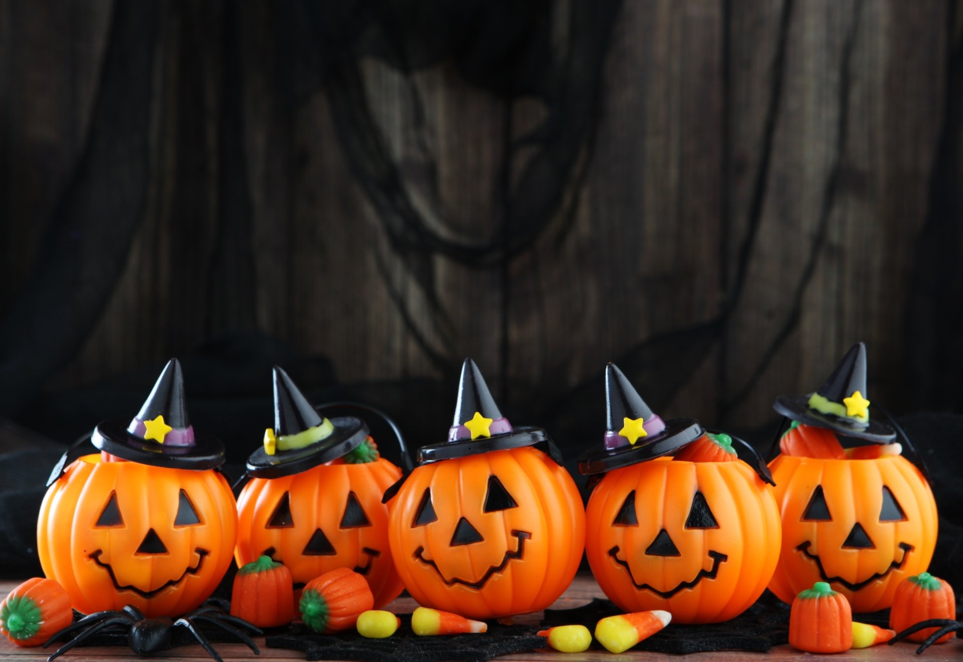 HD Halloween desktop wallpaper featuring five smiling jack-o'-lanterns wearing witch hats, surrounded by small pumpkins and candy against a dark wooden background.