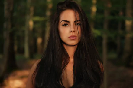 HD desktop wallpaper featuring a brunette woman model with a focused face and soft depth of field, set against a natural forest background.