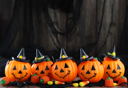 HD Halloween desktop wallpaper featuring five smiling jack-o'-lanterns wearing witch hats, surrounded by small pumpkins and candy against a dark wooden background.