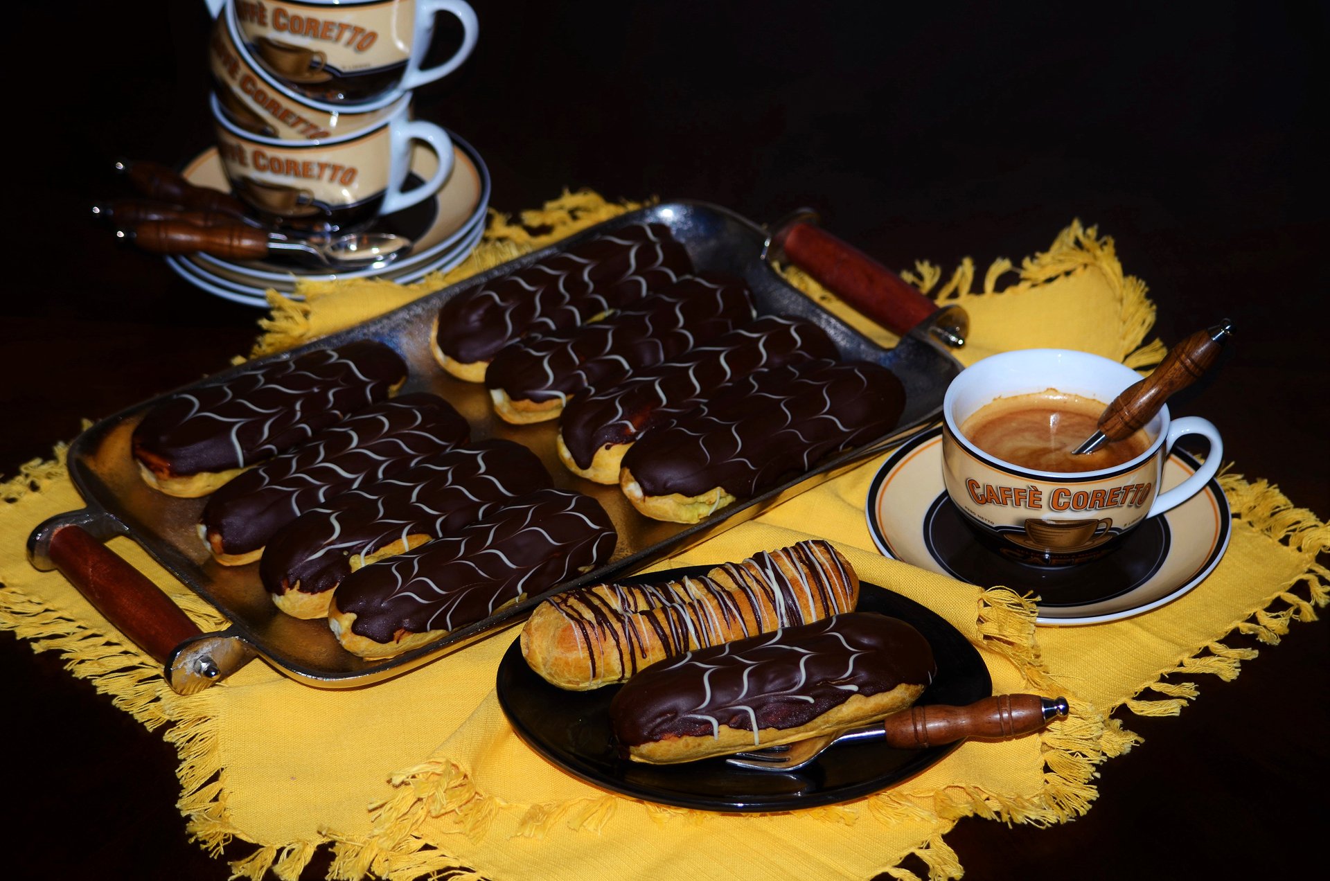 A still life 4K Ultra HD wallpaper featuring chocolate éclairs and a cup of coffee arranged on a yellow cloth, showcasing a rich dessert and pastry scene.