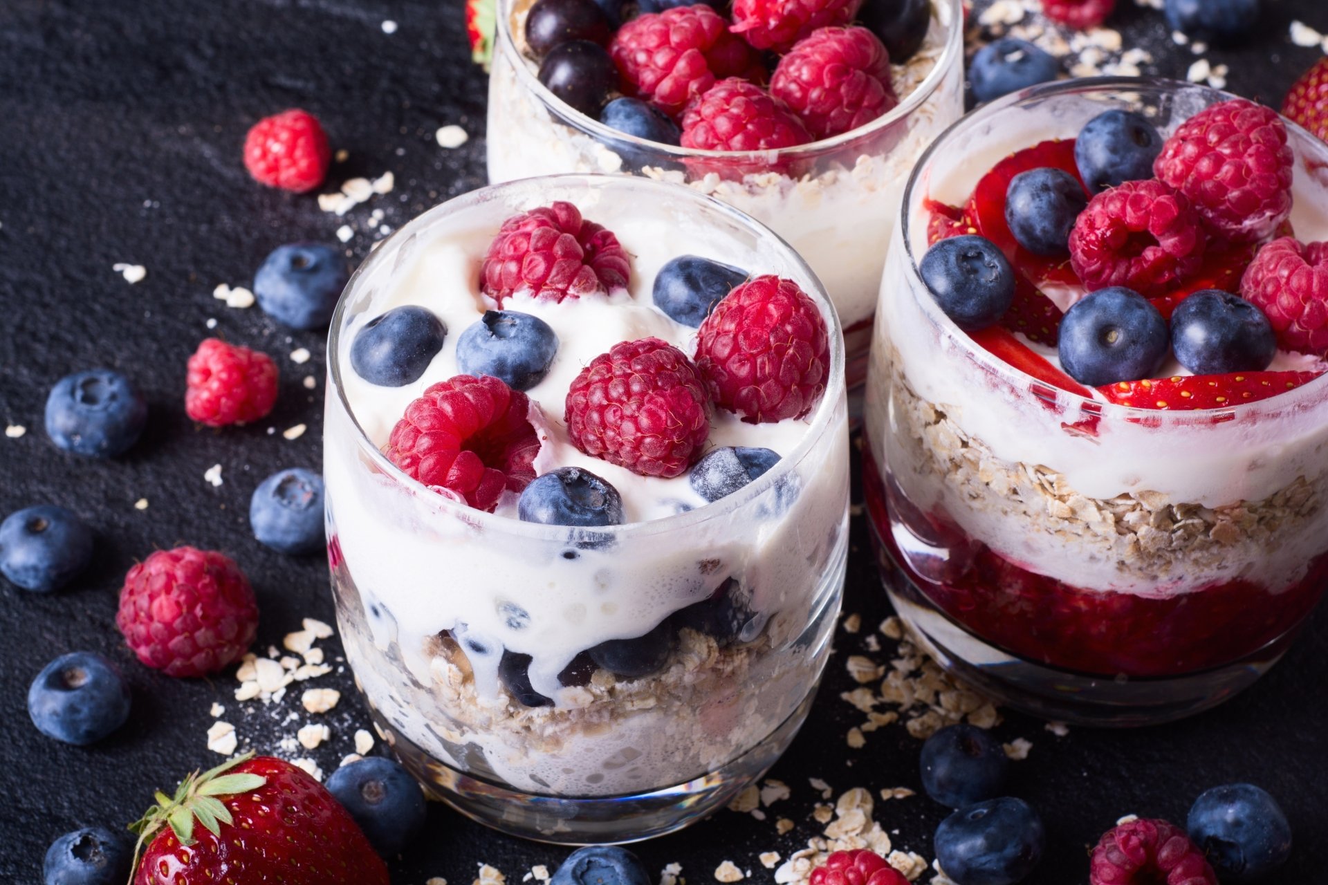 Close-up of three glass cups filled with layered muesli, yogurt, and fresh blueberries and raspberries, styled as a vibrant still life food dessert in 4K Ultra HD.