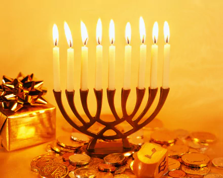 HD desktop wallpaper featuring a lit Hanukkah menorah, gold coins, and a wrapped gift, capturing the holiday spirit with warm candlelight and festive symbols.