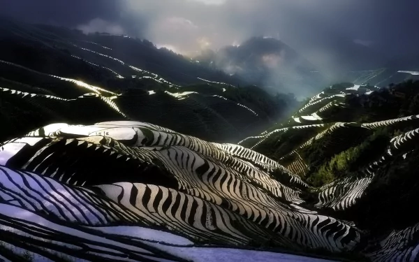 HD desktop wallpaper showcasing a dramatic landscape of man-made rice terraces under a cloudy sky, blending nature and human craftsmanship.