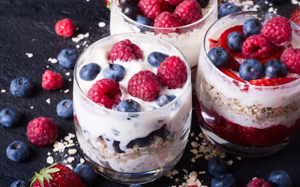 Close-up of three glass cups filled with layered muesli, yogurt, and fresh blueberries and raspberries, styled as a vibrant still life food dessert in 4K Ultra HD.