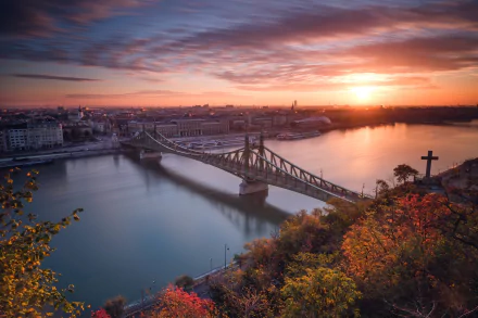 Sunset over Liberty Bridge in Budapest, Hungary, spanning the Danube with city buildings and a glowing sky reflected on the river — HD desktop wallpaper.