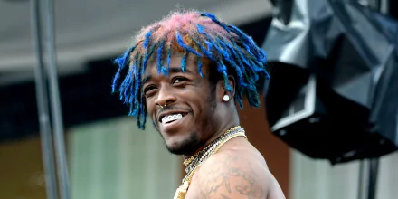 HD desktop wallpaper featuring a smiling person with vibrant blue and pink dreadlocks, diamond earrings, and tattoos.