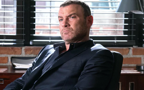 HD desktop wallpaper of a character from Ray Donovan, seated confidently in a room with brick walls and blinds.