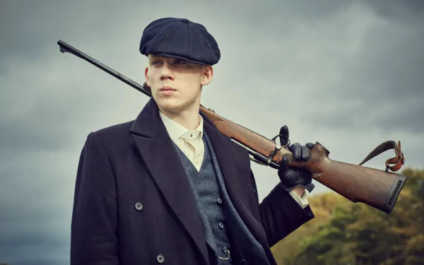 Peaky Blinders TV show 4K Ultra HD PC desktop wallpaper: young man in period coat and flat cap holding a rifle against a brooding, cloudy sky.