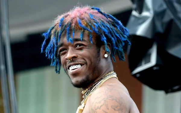 HD desktop wallpaper featuring a smiling person with vibrant blue and pink dreadlocks, diamond earrings, and tattoos.