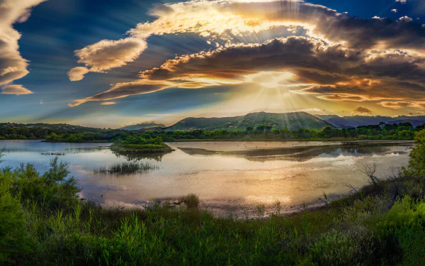 Sunbeams break through clouds over a serene Corsica lake surrounded by lush greenery, captured in stunning HD nature scenery for a PC desktop wallpaper.