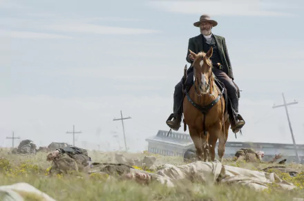 HD wallpaper featuring a scene from Godless with a character riding a horse across a prairie with crosses and a building in the background.