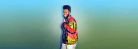 HD wallpaper of a smiling person in a colorful jacket on a gradient background, tagged with Khalid.