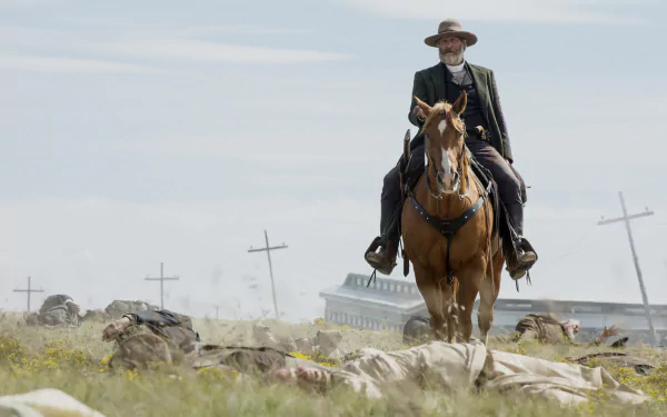 HD wallpaper featuring a scene from Godless with a character riding a horse across a prairie with crosses and a building in the background.