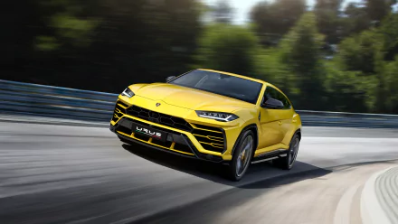 A sleek yellow Lamborghini Urus SUV driving on a curvy road, set against a blurred natural background. HD desktop wallpaper and background.