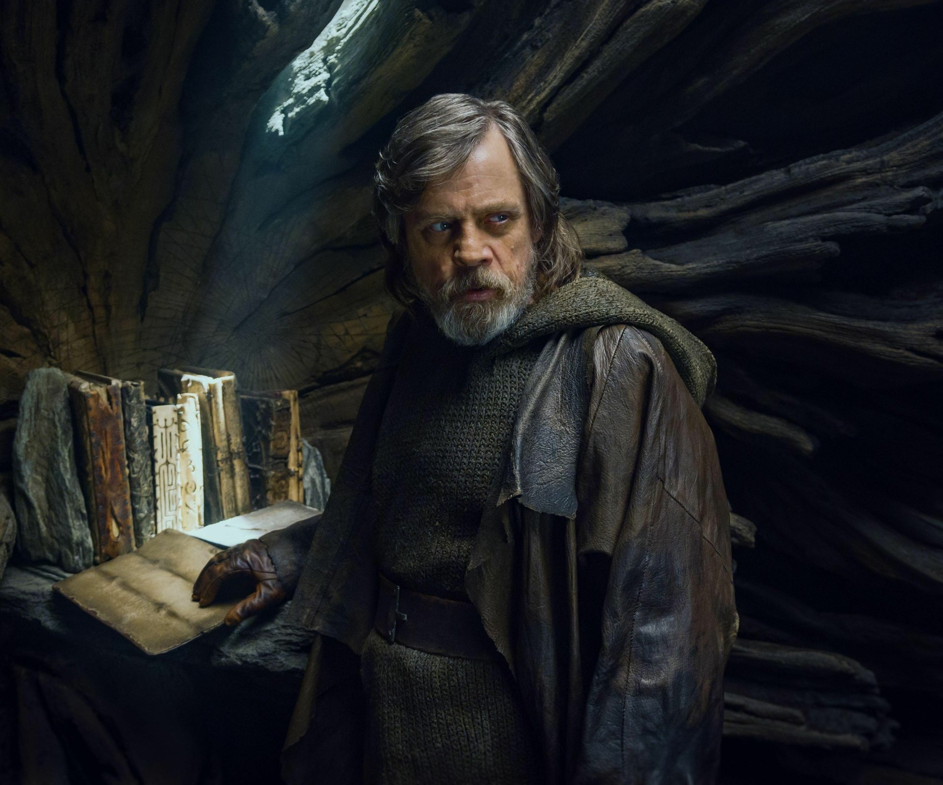 Luke Skywalker from Star Wars: The Last Jedi stands in a dimly lit cave, holding a book, captured in this 4K Ultra HD PC desktop wallpaper.