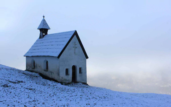 4K Ultra HD PC desktop wallpaper and background: a small snow-covered chapel on a winter hillside, a solitary religious church silhouette beneath a pale, misty sky.